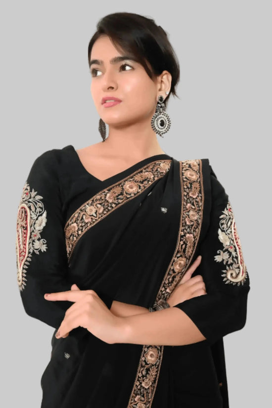 Woman wearing a black saree with intricate gold embroidery on a white background